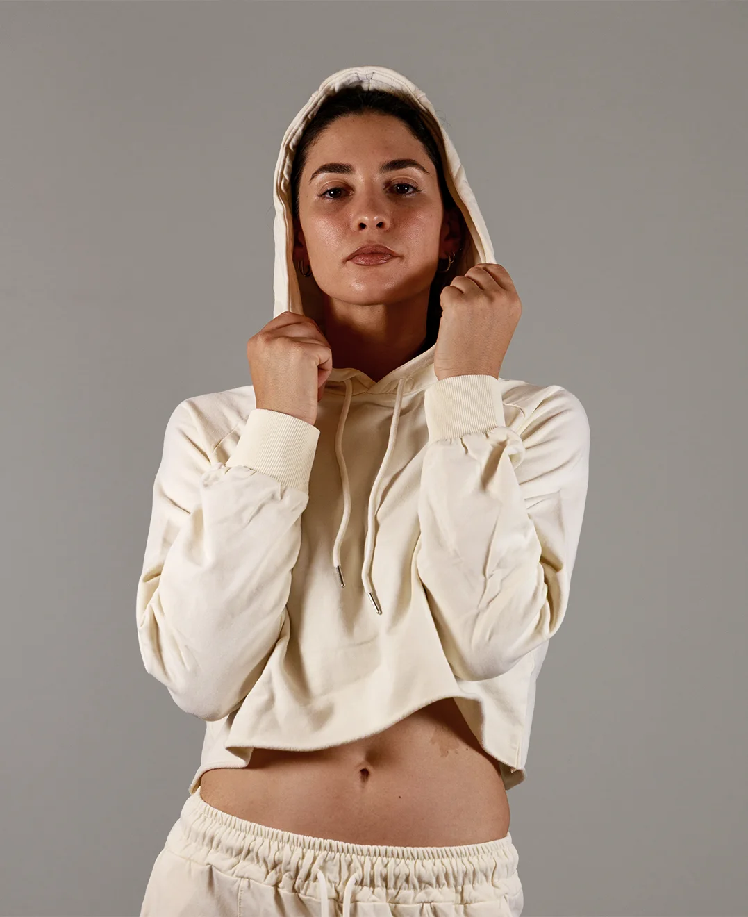 Giovane modella indossa felpa Crop con cappuccio alzato per Pilates, color burro, modello Akira, della linea di abbigliamento Be You