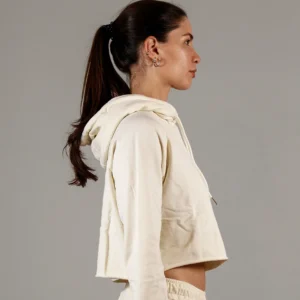 Giovane modella di profilo indossa felpa Crop con cappuccio per Pilates, color burro, modello Akira, della linea di abbigliamento Be You