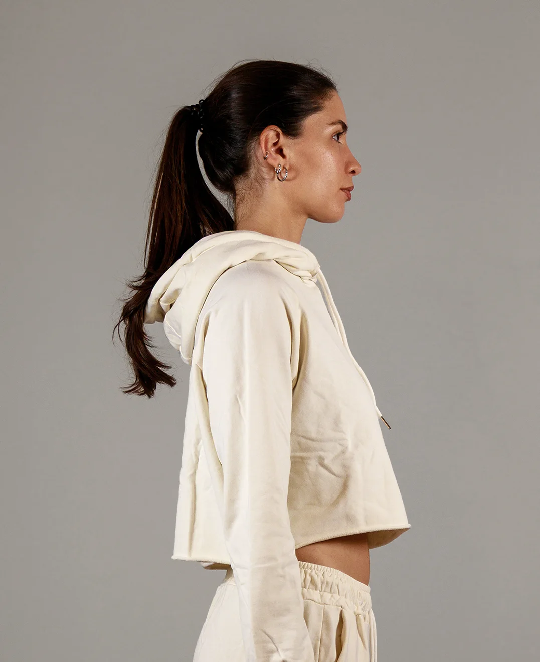 Giovane modella di profilo indossa felpa Crop con cappuccio per Pilates, color burro, modello Akira, della linea di abbigliamento Be You