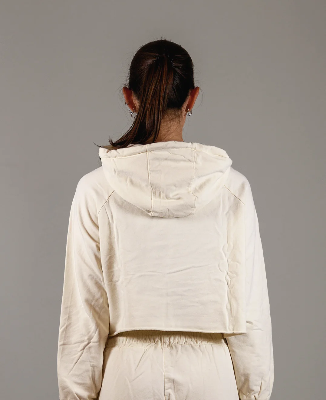 Giovane modella di spalle indossa felpa Crop con cappuccio per Pilates, color burro, modello Akira, della linea di abbigliamento Be You