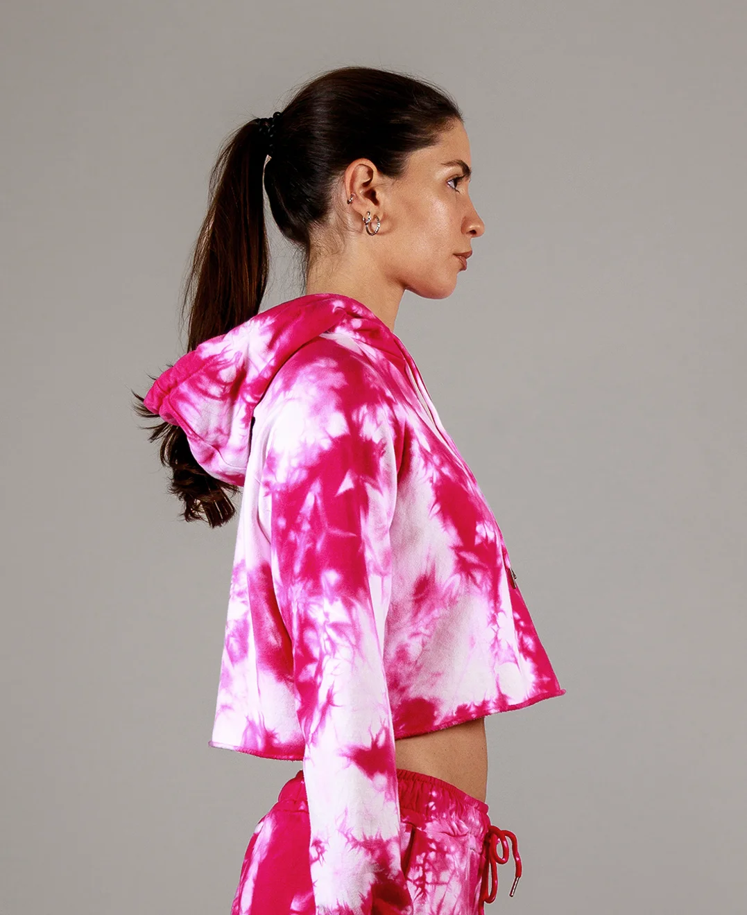 Giovane modella di profilo indossa felpa Crop con cappuccio per Pilates, fucsia Tie-Dye, modello Akira, della linea di abbigliamento Be You Firenze